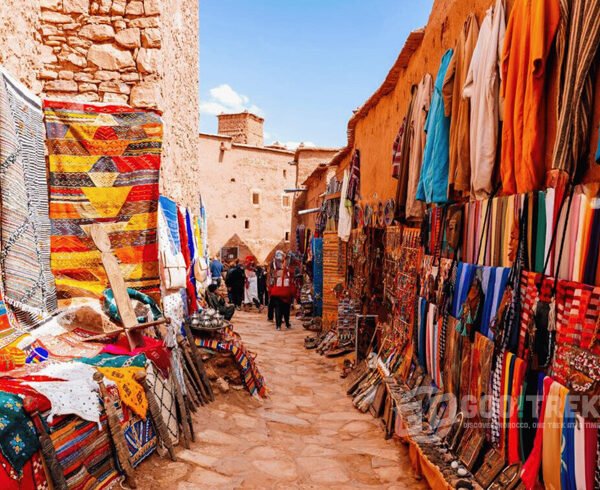 Colorful local market in Ait Ben Haddou showcasing handmade Moroccan rugs, textiles, and crafts during a day trip from Marrakech to Ouarzazate.
