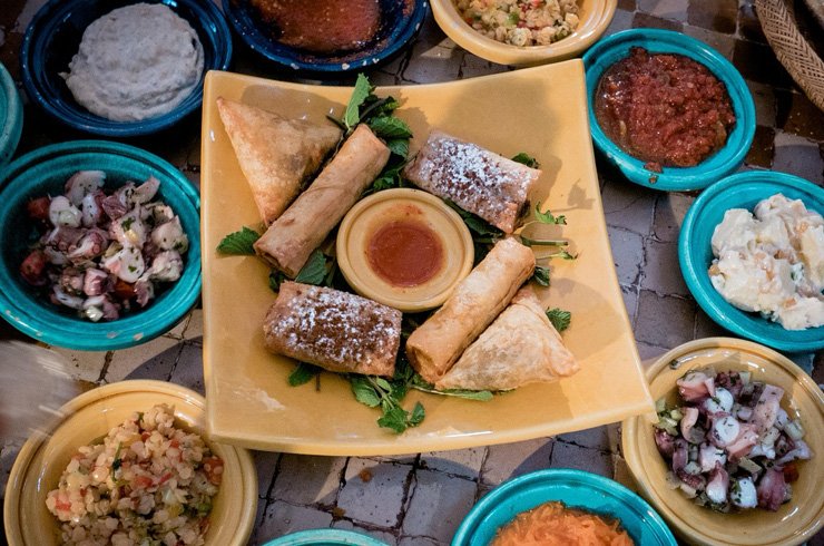 Close-up of a traditional Moroccan tagine dish served with vegetables and lamb, surrounded by couscous, mint tea, and colorful spices in a warm and authentic Moroccan setting